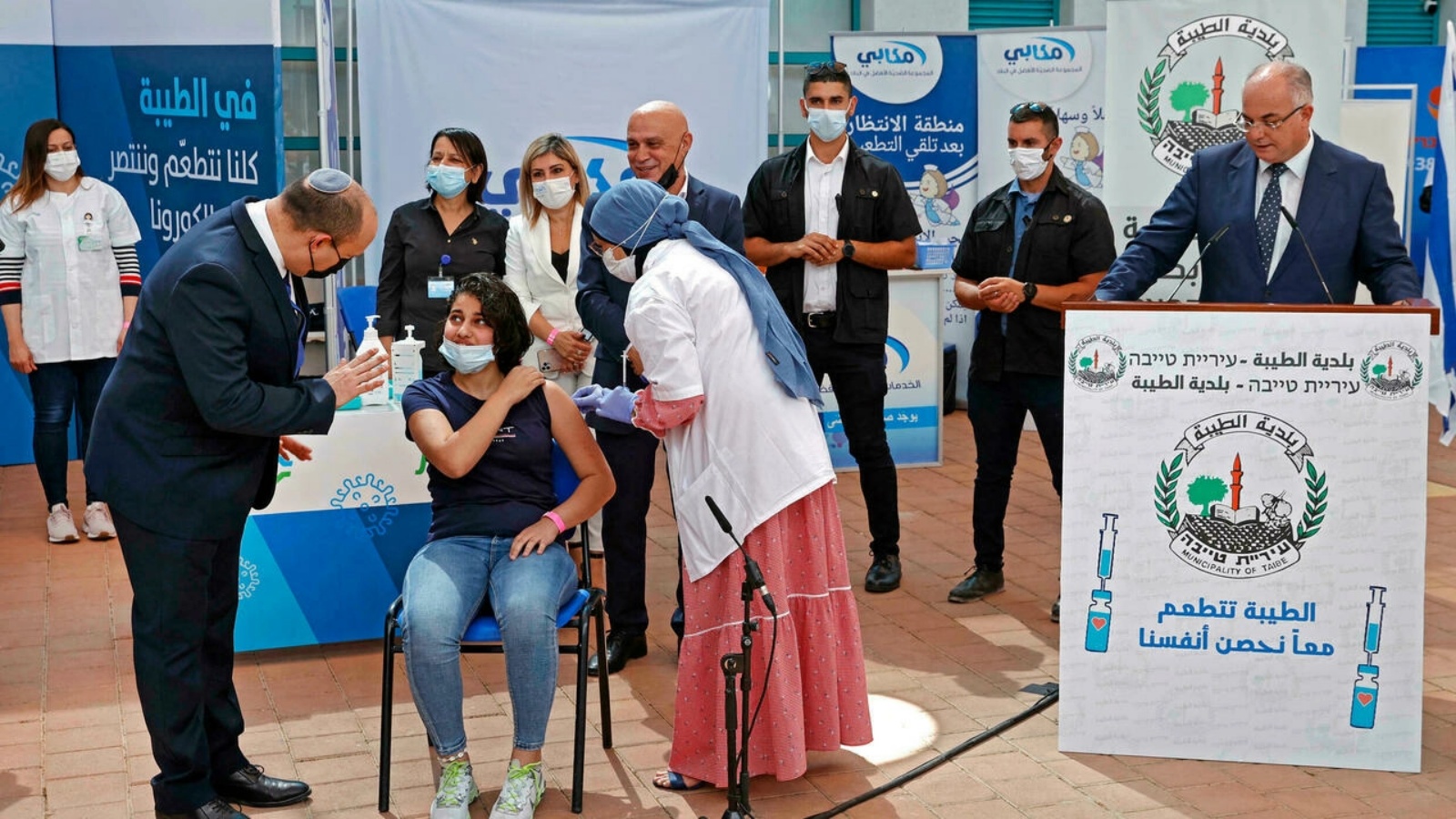 رئيس الوزراء الإسرائيلي نفتالي بينيت يتحدث إلى شابة أثناء تلقيها لقاح فيروس كورونا في مدرسة ثانوية بمدينة الطيبة. في 19 آب/أغسطس 2021. 