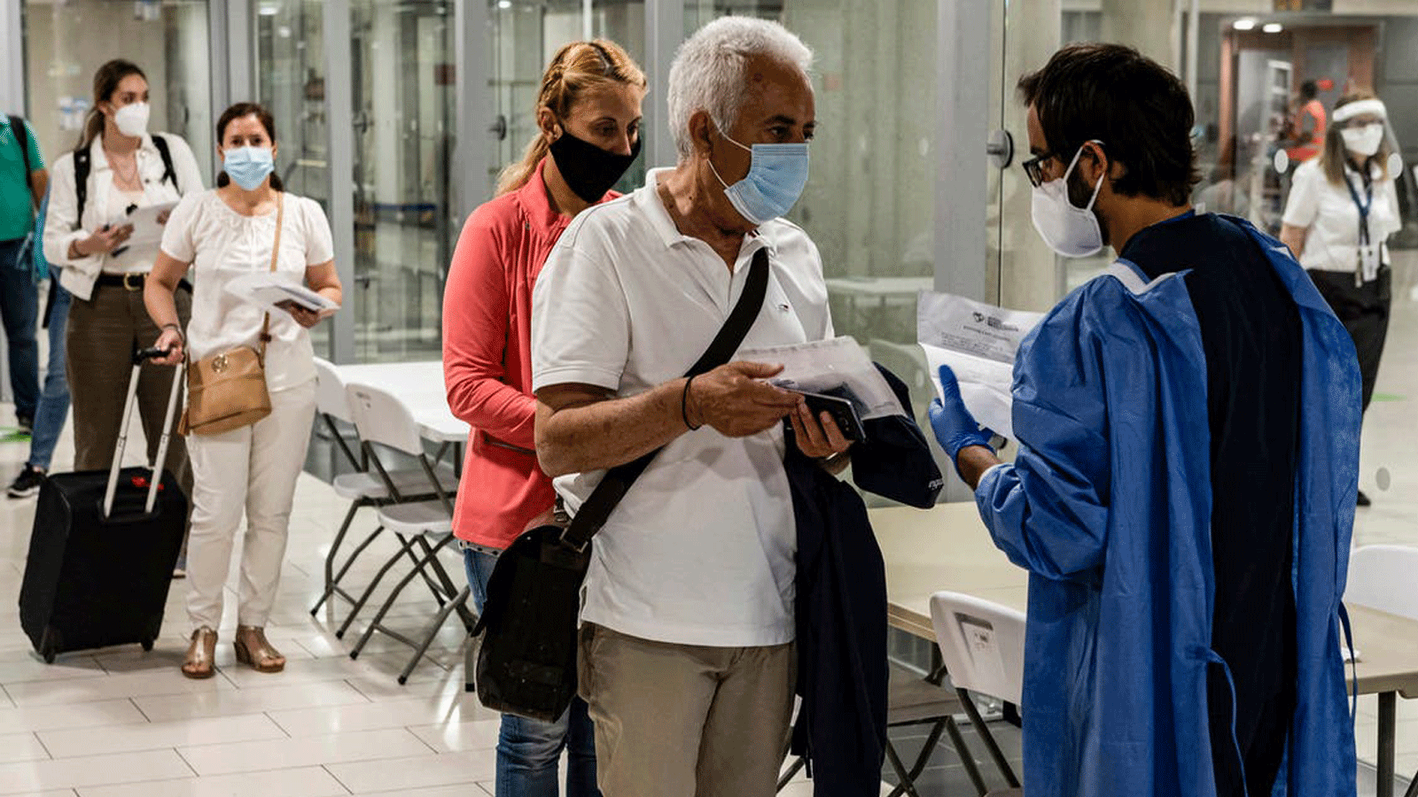 المسعفون يتحققون من وثائق المسافرين مرتدين الأقنعة الذين يصلون إلى مطار لارنكا الدولي في قبرص في 9 حزيران/ يونيو 2020، قبل أن يتم فحصهم بحثًا عن أعراض COVID-19 وهم في طريقهم إلى مراقبة جوازات السفر.