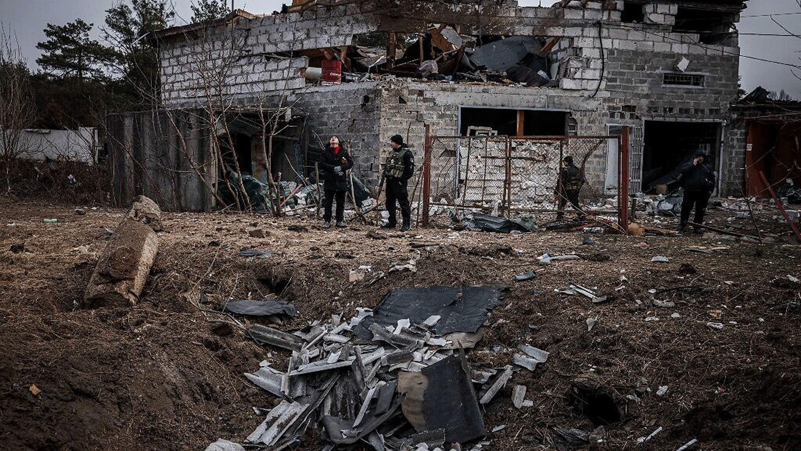 عناصر من الشرطة وسكان يقفون بجوار حفرة قذيفة أمام منزل دمره القصف الأخير في ضواحي كييف في 12 مارس / آذار 2022 