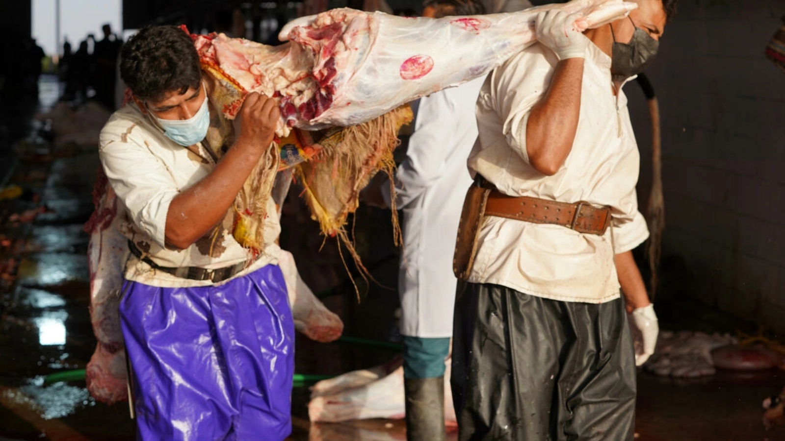 رجلان يحملان قطعة من اللحم في أحد مسالخ النجف في جنوب العراق في 26 مايو 2022
