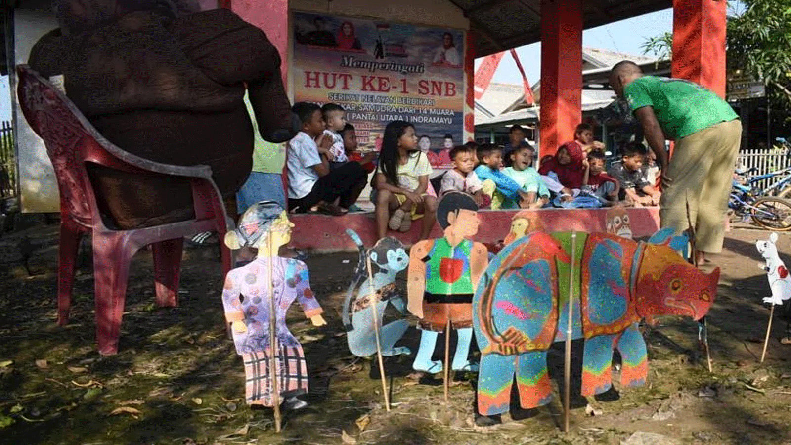 المعلم المتقاعد سامسودين(Samsudin) (إلى اليمين) يعلّم الأطفال كيفية الحفاظ على الحيوانات باستخدام الدمى المصنوعة من الورق المقوى في قرية سيمارا كولون(Cemara Kulon)، في إندرامايو(Indramayu).