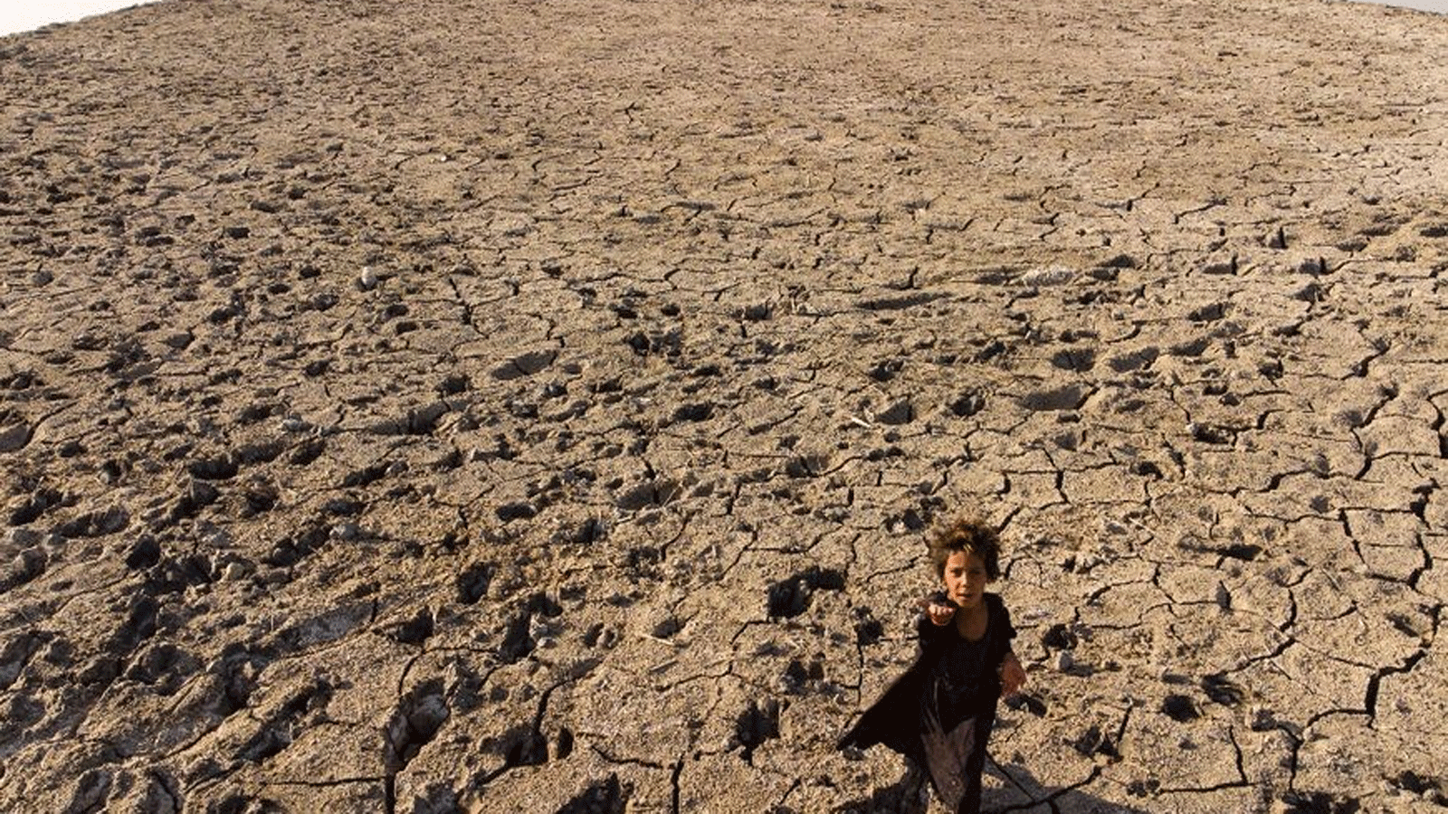 طفلٌ يسير عبر الأهوار الجافة في جنوب محافظة ذي قار في 23 آب\أغسطس 2022 حيث تضرب موجات الحر والجفاف والعواصف الرملية في العراق، أحد أكثر البلدان المهددة بالتغيّر المناخي
