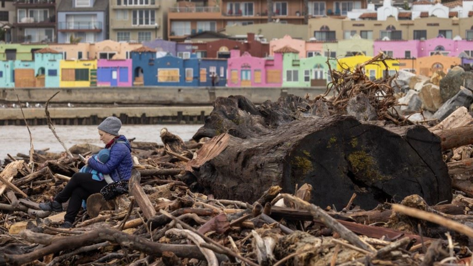 امرأة تجلس مع طفلها بين أشجار جرفتها العواصف الأخيرة في المحيط قبل ان تستقر على الشاطئ في كابيتولا بكاليفورنيا 15 يناير 2023