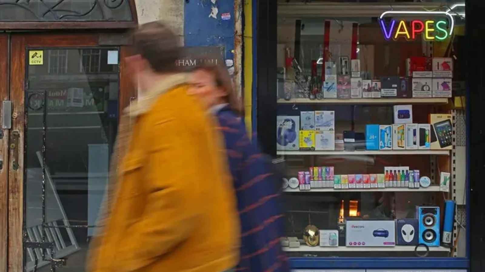 أشخاص يسيرون بالقرب من بائع جرائد يعلن عن بيع السجائر الإلكترونية في ستريثام هيل، في جنوب لندن، في 1 نيسان (أبريل) 2023