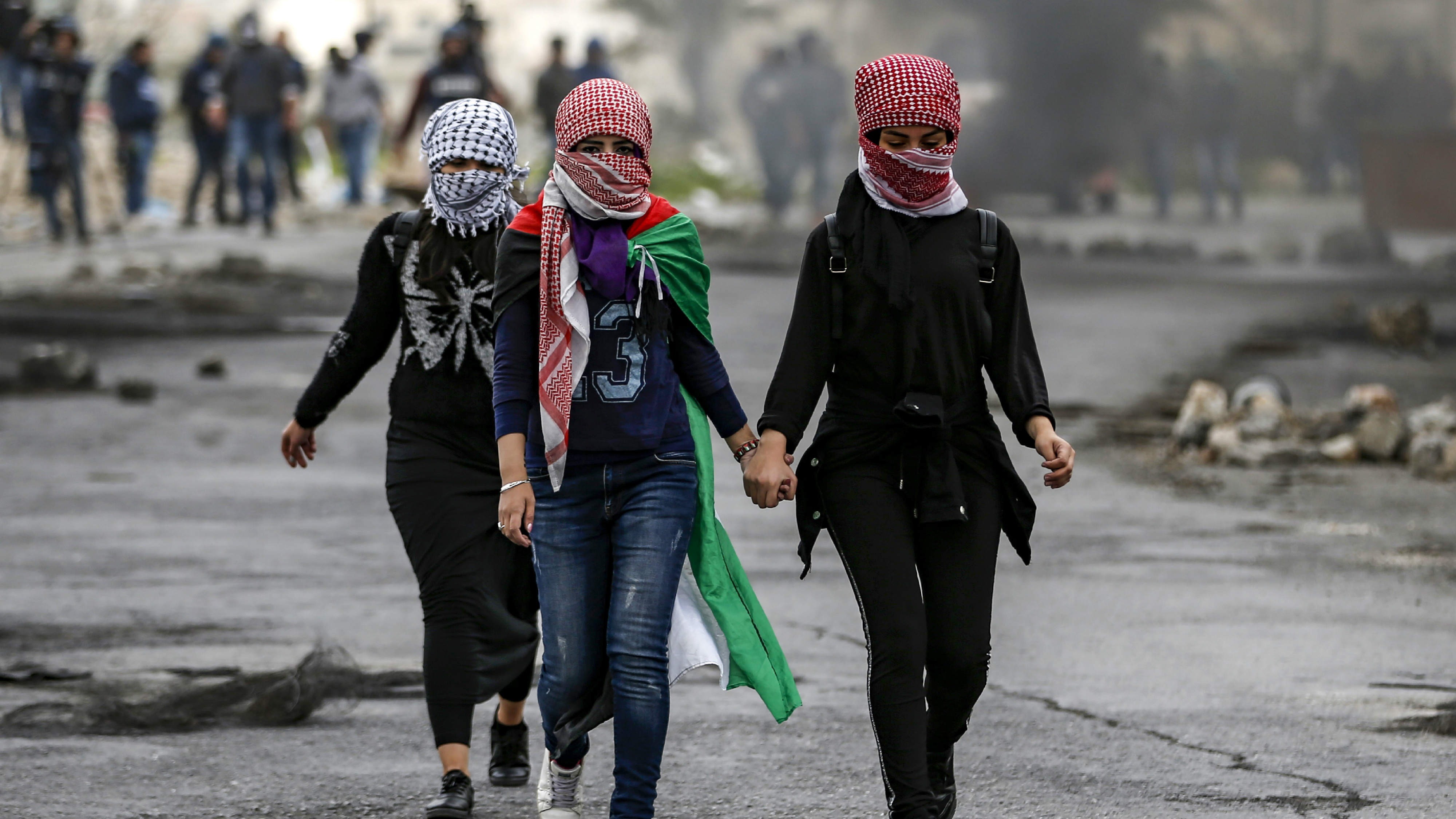 فتيات فلسطينيات وجوههن مغطاة بالكوفيات التقليدية ذات المربعات يسيرن خلال اشتباكات مع القوات الإسرائيلية في أعقاب مظاهرة بمناسبة يوم الأرض في الضفة الغربية