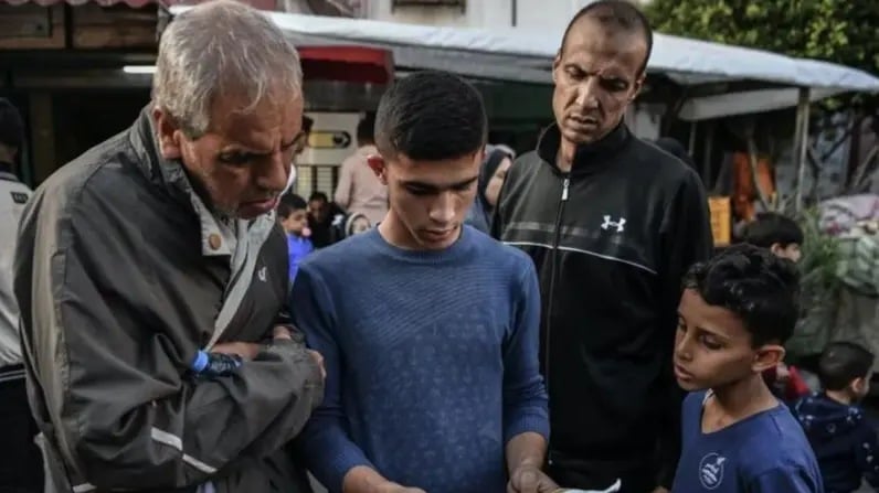 رجلان وصبيان في أحد شوارع غزة يقرأون منشوراً يحتوي على تحذير للجيش الإسرائيلي من أجل الإخلاء