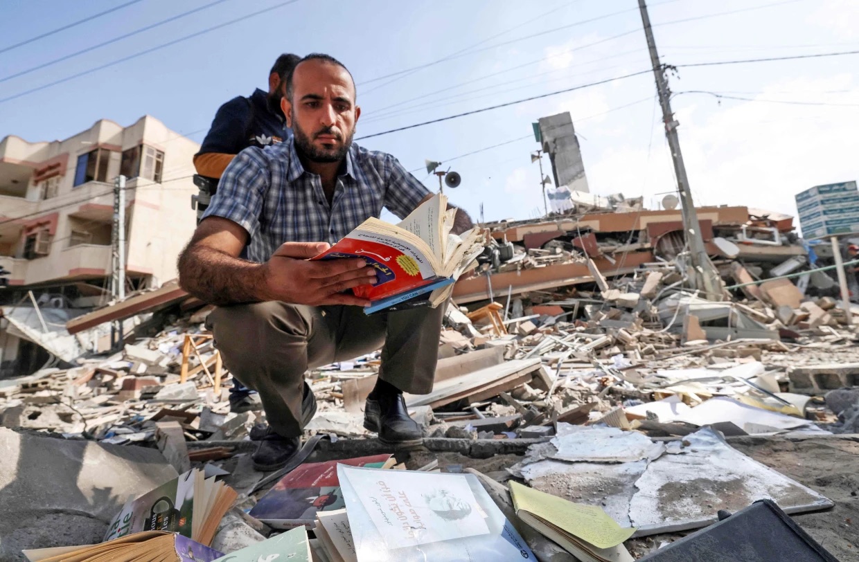 فلسطيني يحمل كتابًا استخرجه من تحت أنقاض مبنى كحيل الذي كان يضم مكتبة سمير منصور في مدينة غزة