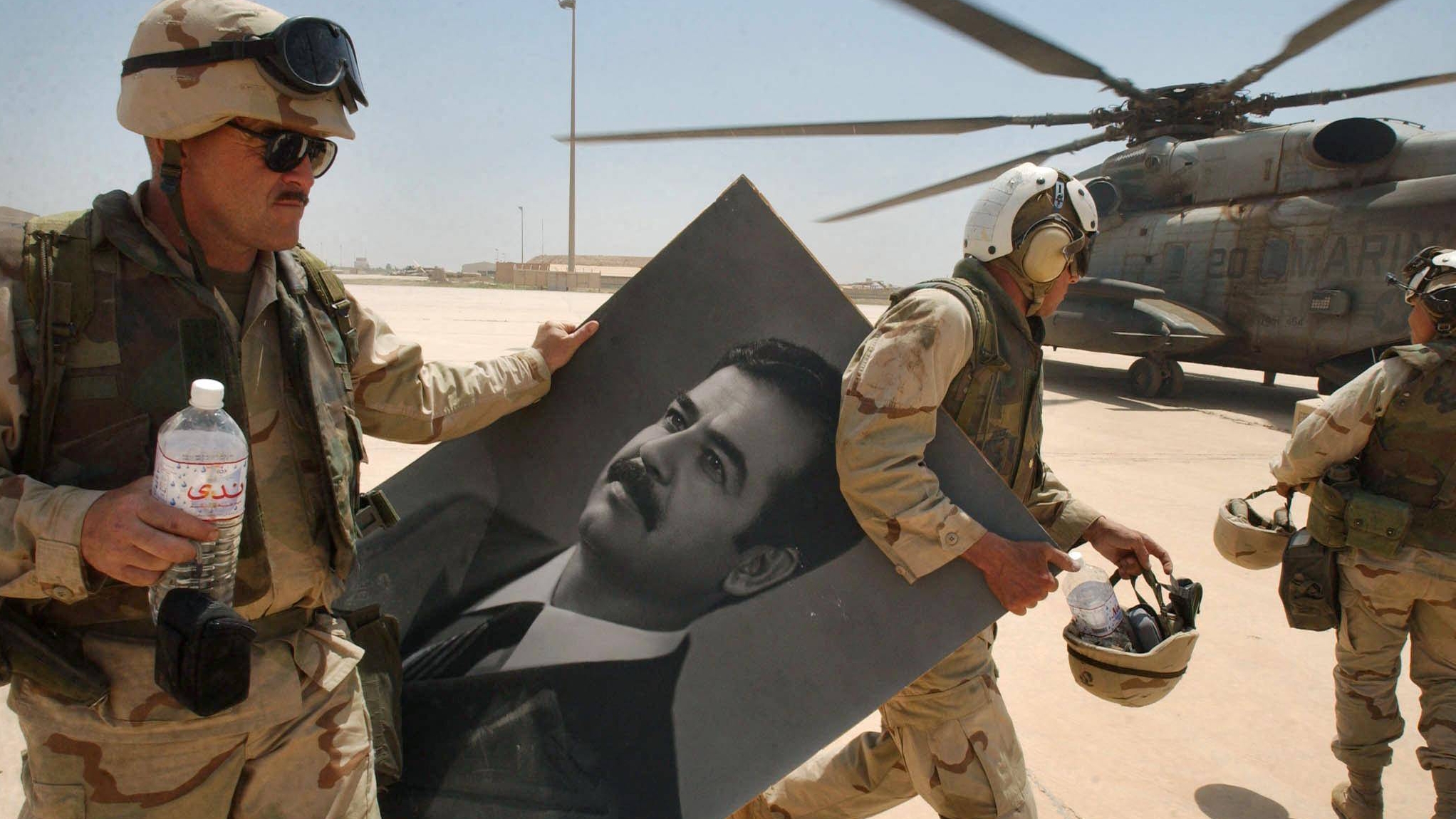 جنود مشاة البحرية الأميركية يحملون صورة الرئيس العراقي المخلوع صدام حسين في مطار صدام الدولي في بغداد في نيسان (أبريل) 2003