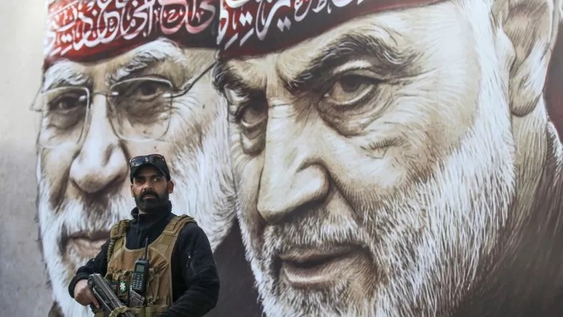 عنصر من إحدى المليشيات الموالية لإيران أمام ملصق لقاسم سليماني (اليمين) والقائد العراقي أبو مهدي المهندس في بغداد في العراق، في 13 كانون الثاني (يناير) 2024