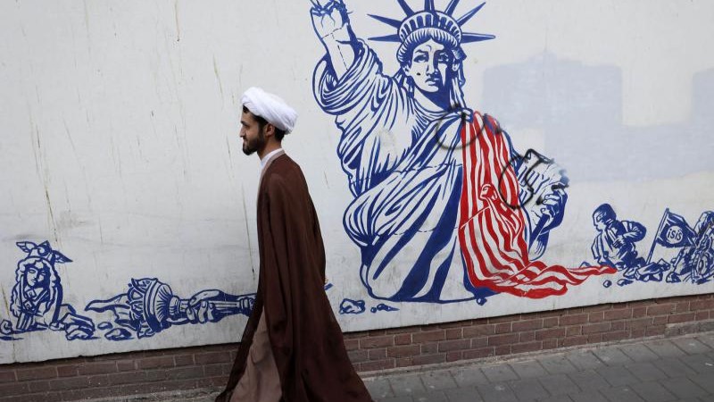 رجل دين إيراني يسير أمام لوحة جدارية مناهضة للولايات المتحدة على جدار السفارة الأميركية السابقة في طهران
