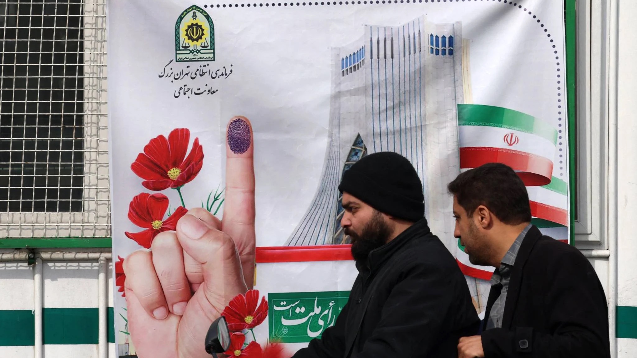 رجلان يمران في طهران بالقرب من إعلان لانتخابات منتظرة تصاحبها الكثير من الإشكاليات المتعلقة بالنزاهة