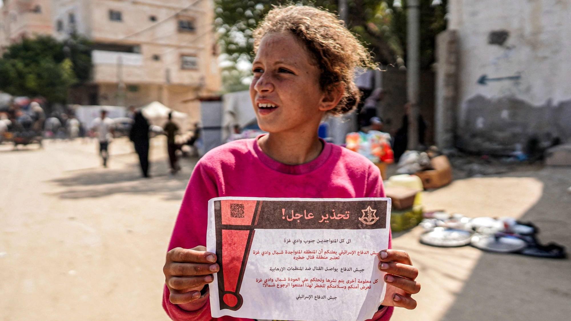 طفلة فلسطينية تحمل منشوراً ألقاه الجيش الإسرائيلي على دير البلح في قطاع غزة يحذر من عودة النازحين للشمال