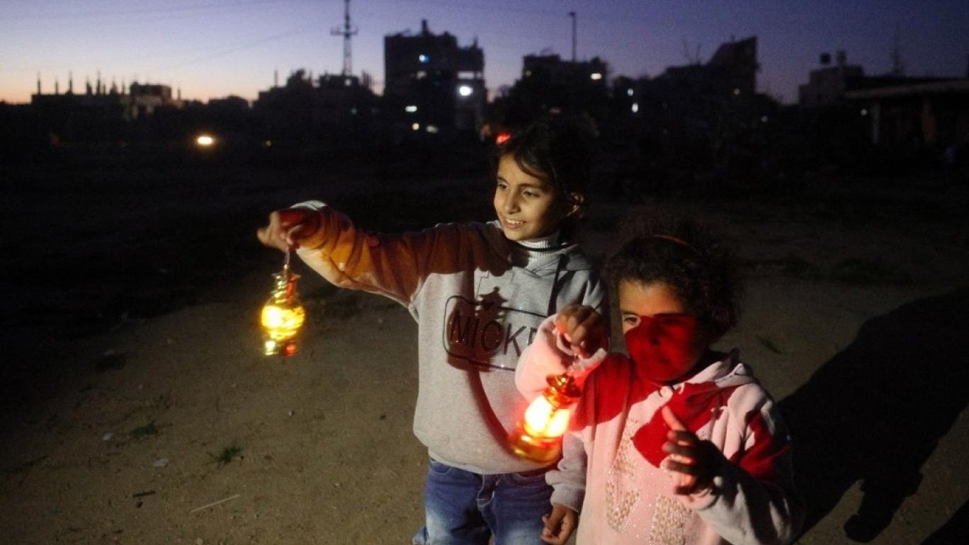 فتيات فلسطينيات يحملن فوانيس رمضان التقليدية أثناء احتفالهن باليوم الأول من الشهر في مخيم البريج للاجئين وسط قطاع غزة مطلع آذار (مارس) 2025