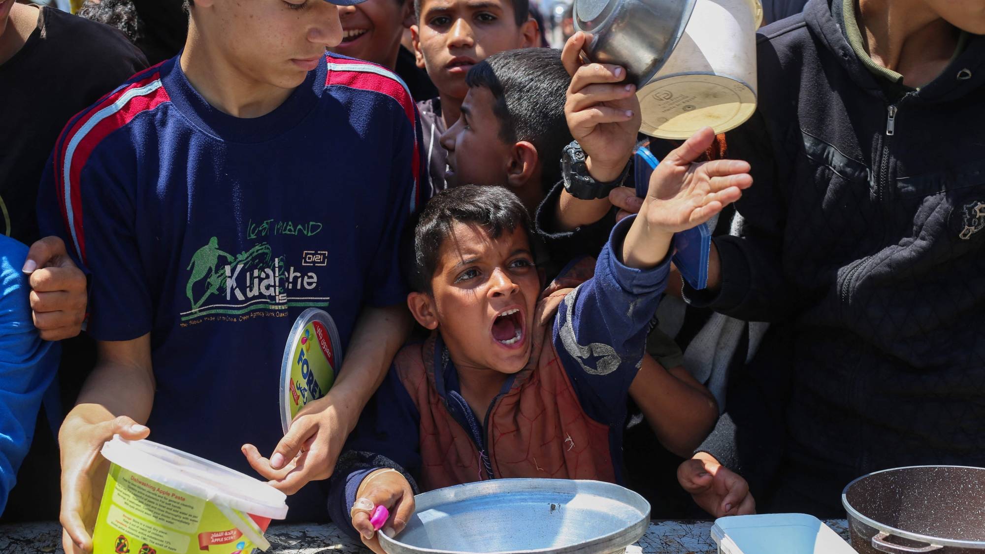 صبي فلسطيني مع أقرانه في أثناء الحصول على الطعام من مطبخ خيري بمخيم النصيرات وسط غزة يوم الأربعاء