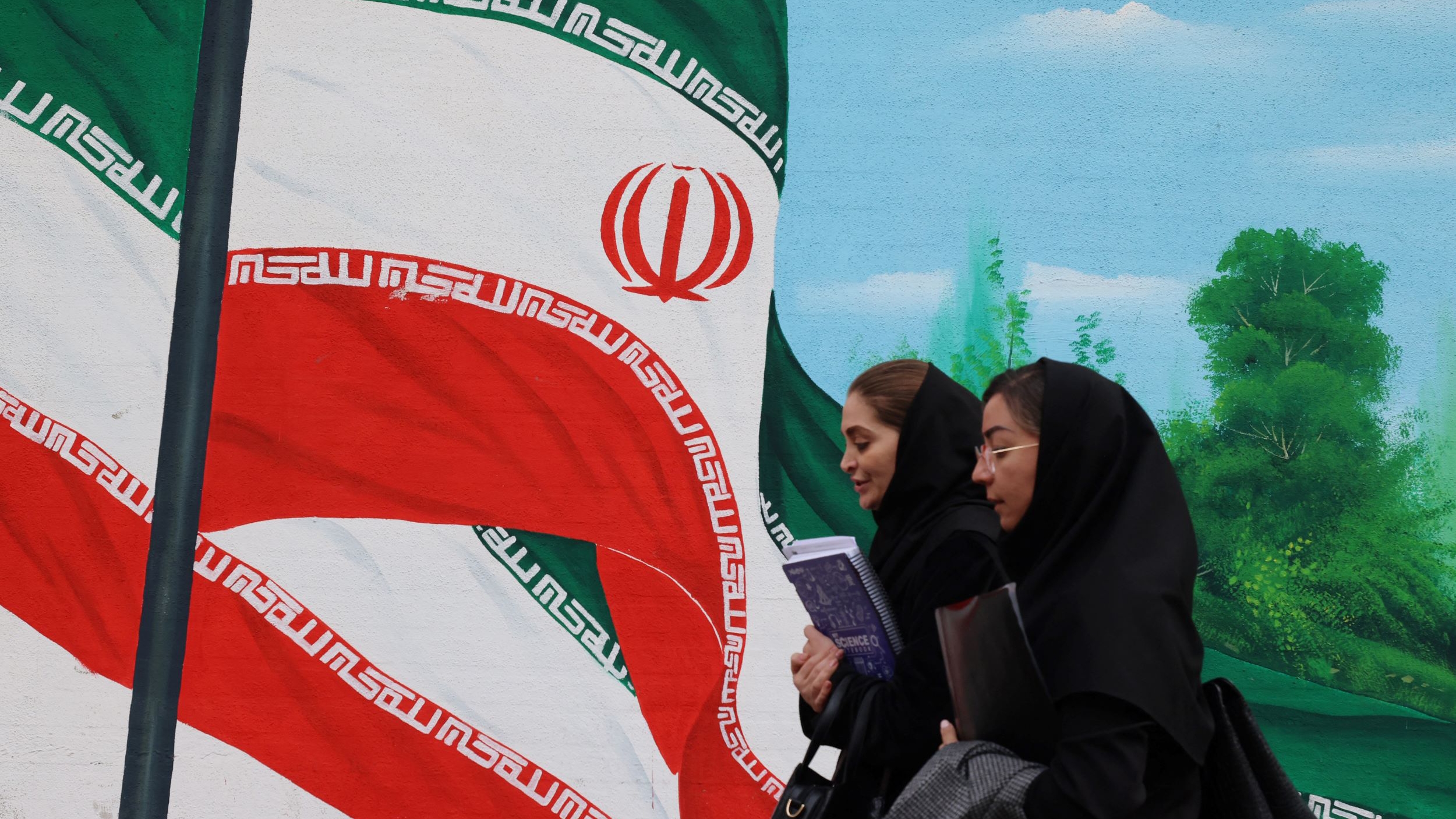 إيرانيتان تمران أمام جدارية تحمل أعلامًا إيرانية في طهران في 26 تشرين الثاني (نوفمبر) 2024