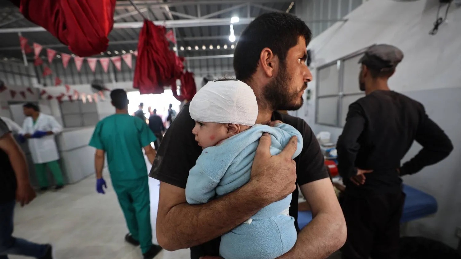 رجل يحمل طفلاً مصاباً بعد تلقيه العلاج في مستشفى العودة بمخيم النصيرات للاجئين وسط غزة