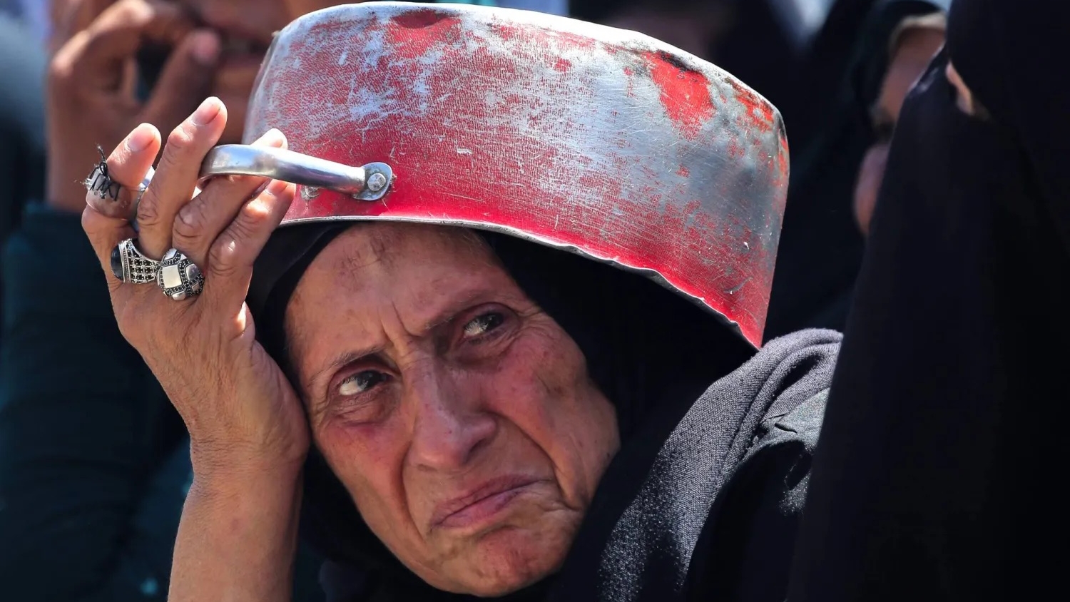 سيدة فلسطينية تستخدم وعاء لحمايتها من الشمس خلال انتظارها الحصول على طعام في نقطة توزيع بمخيم النصيرات وسط قطاع غزة