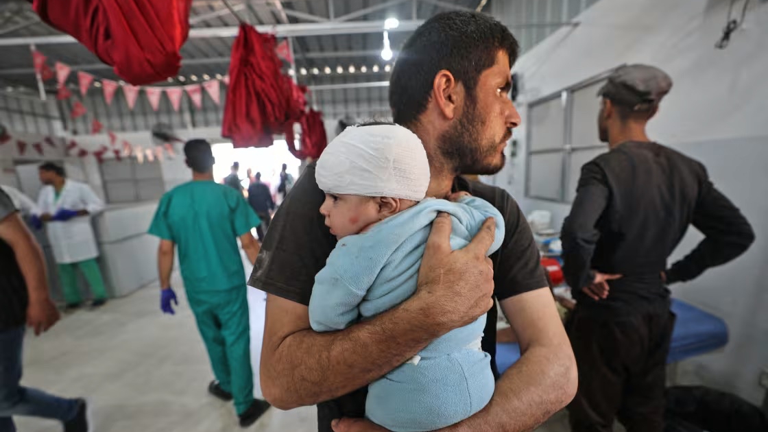رجل يحمل طفلاً مصاباً في مستشفى العودة في أيار (مايو) 2025
