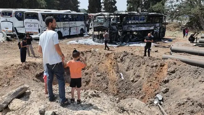 مارة أمام حفرة ضخمة في موقع سقوط صاروخ إيراني في محطة حافلات في هرتسليا، بالقرب من تل أبيب، في 17 حزيران (يونيو) 2025