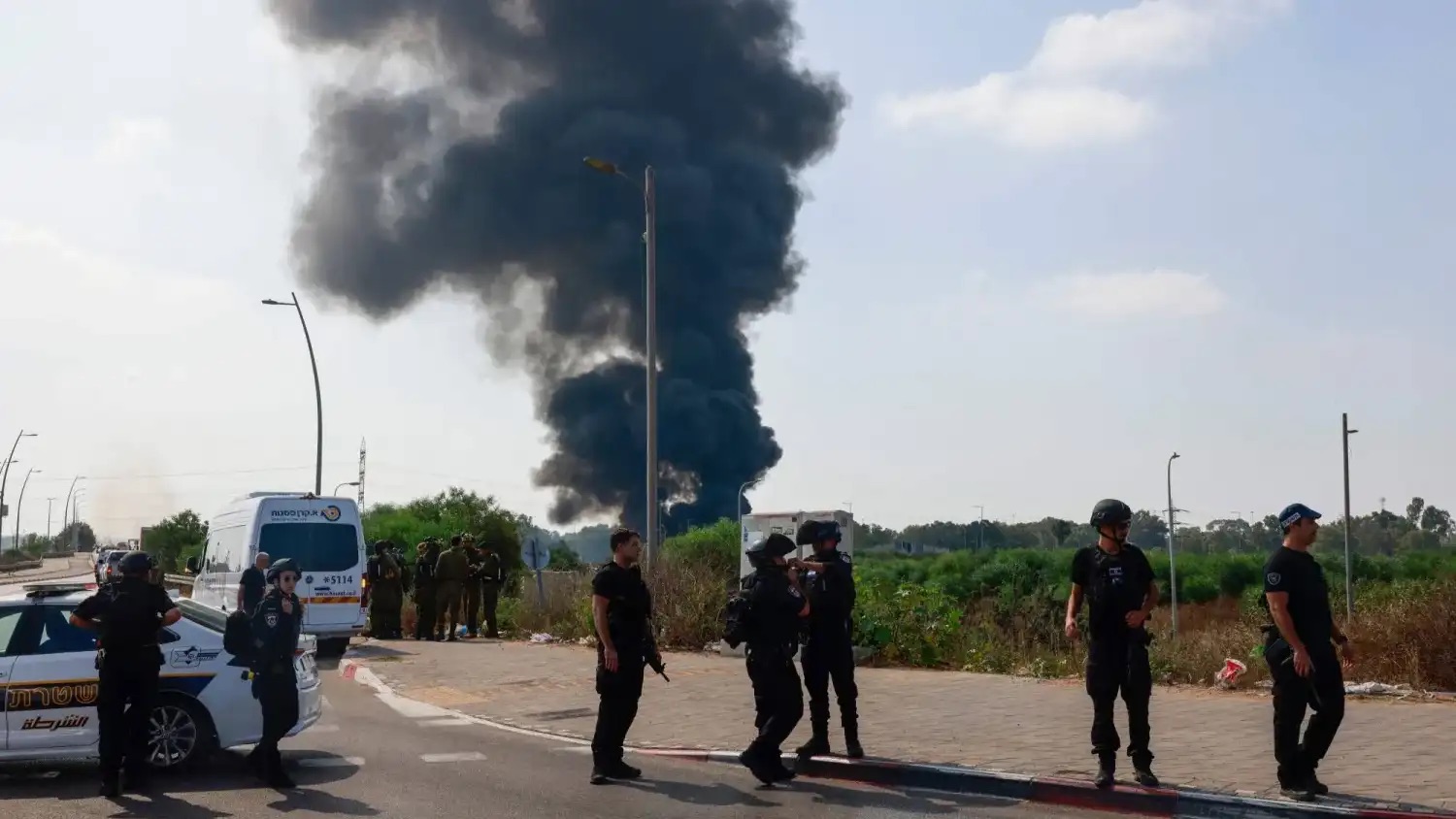 عناصر من الشرطة الإسرائيلية تقف بينما يتصاعد دخان جراء غارات إيرانية على موقع في هرتسليا قرب تل أبيب