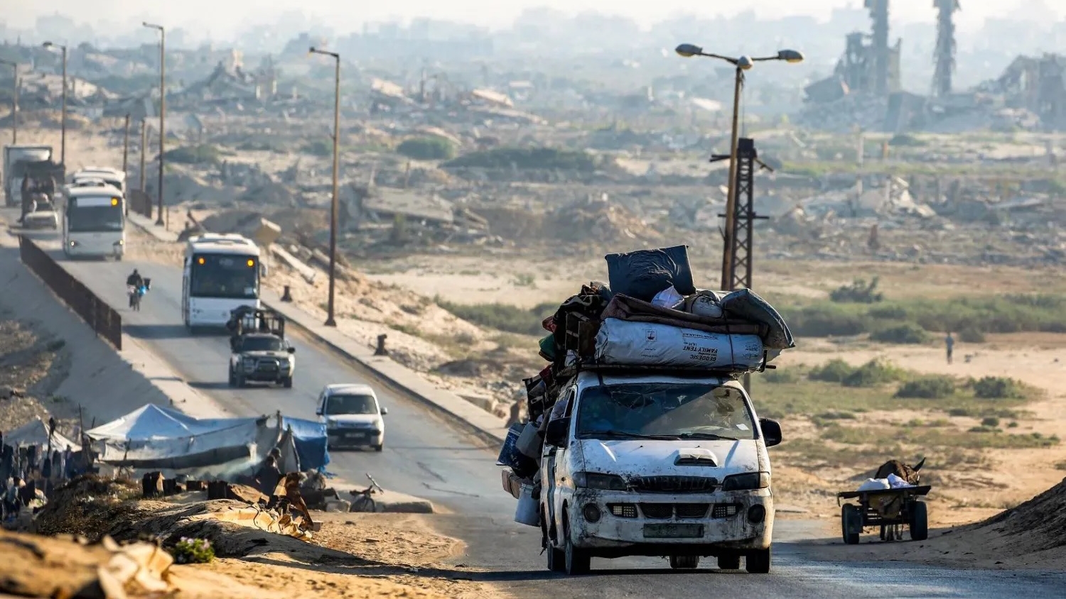 مركبات محملة بأغراض تمر بجانب مبانٍ مدمرة على طول الطريق الساحلي عبر مخيم النصيرات للاجئين الفلسطينيين