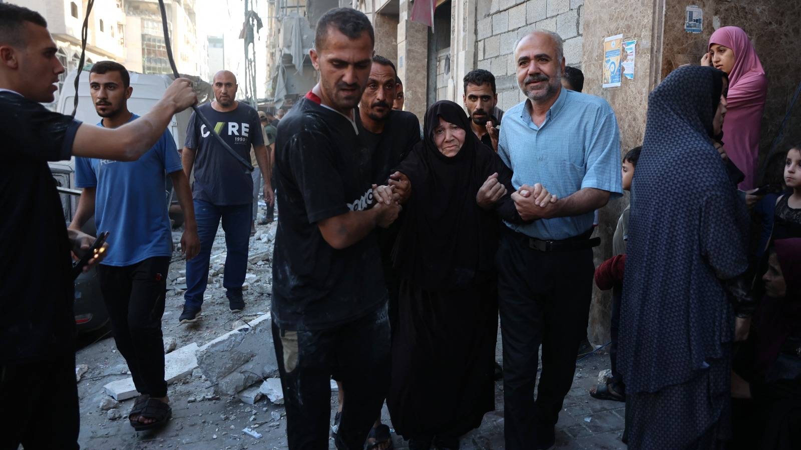 فلسطينيون يساعدون امرأة مُسنة في موقع غارةٍ إسرائيليةٍ استهدفت عدة مبانٍ بحي الرمال بمدينة غزة