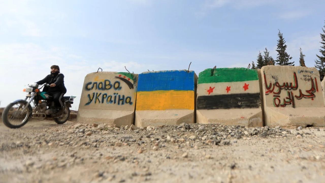 سائق دراجة نارية يمر عبر كتل إسمنتية مطلية بعلمي أوكرانيا وسوريا بالقرب من مدينة الباب