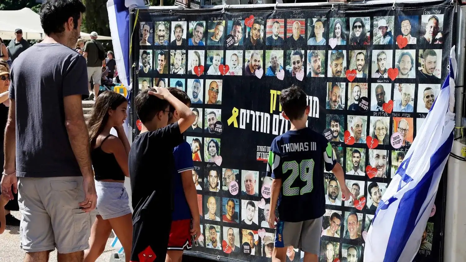 رجل وأولاد يتفرجون على صور للرهائن الإسرائيليين في «ساحة الشهداء» بتل أبيب السبت