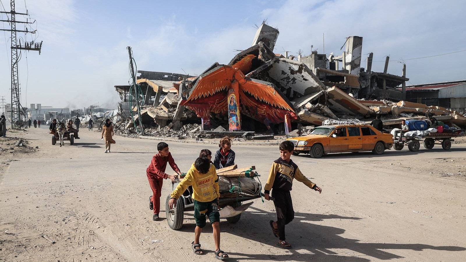 أطفال يجرون عربة أمام جدارية على مبنى مدمر في مخيم المغازي للاجئين خارج دير البلح
