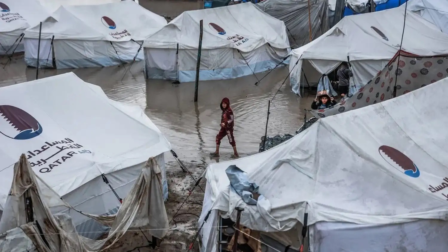 طفل يسير في زقاق غمرته المياه بمخيم مؤقت يؤوي نازحين فلسطينيين بعد هطول أمطار غزيرة في حي الزيتون الشهر الحالي