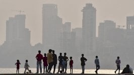 مجموعة من الأطفال والشبان يقفون قرب شاطئ تقابله أبنية مرتفعة في مشهد ضبابي يبدو أنه لسماء ملوثة. - Getty Images