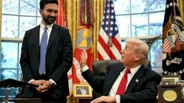 يظهر ممداني واقفاً بجانب ترامب، الجالس خلف مكتبه في المكتب البيضاوي. كلاهما يبتسمان، ويمد ترامب يده ليداعبه مازحاً. يرتدي ترامب بدلة رسمية تبدو سوداء اللون وقميصاً أبيض وربطة عنق حمراء. ممداني يرتدي بدلة رسمية سوداء وقميصاً أبيض وربطة عنق زرقاء. - Getty Images