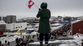 امرأة تلوّح بعلم غرينلاند تقف على ربوة تكسوها الثلوج، بينما يشارك سكان في احتجاج، بنوك عاصمة الجزيرة ضد مطالبة الرئيس دونالد ترامب بالتنازل عن الجزيرة القطبية الشمالية للولايات المتحدة. - Reuters