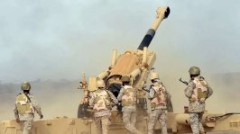 جنود سعوديون يقفون أمام وحدة مدفعية يطلقون قذائف نحو اليمن من موقع قرب الحدود السعودية اليمنية في جنوب غربي السعودية، عام 2015، ويرتدون زياً عسكرياً وكذلك خوذات عسكرية. - Getty Images