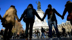 أشخاص يمسكون أيدي بعضهم البعض تضامنا مع ضحايا هجمات باريس 2015 أمام مبنى مسرح الباتاكلان في برايس - Reuters