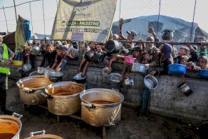 صورة لأشخاص من خلف سور يمدون أوانيهم الفارغة في انتظار نصيب من الأكل الساخن الذي تقدمة المطابخ المجتمعية. - Getty Images