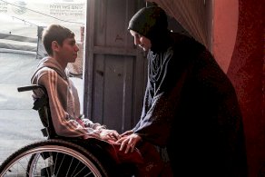 أحد الفتية مبتور الساقين من ضحايا الحرب في غزة يجلس على كرسي متحرك وبمواجهته أمه التي تعتني به بعد أن أصبح معوقا - Getty Images