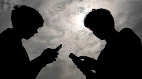 صورة لخيال طفليين لاتبدو ملامحهما يقفان وجها لوجه وكل منهما يتصفحه هاتفه النقال - Getty Images