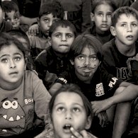 صورة بالأبيض والأسود لأطفال صغار يجلسون على الأرض وينظرون إلى الأعلى، وقد رُسم على وجه أحدهم شارب ولحية بالقلم. - BBC