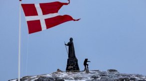 رجل يمشي قرب تمثال هانز إيغيدي في نوك بينما يرفرف العلم الدنماركي بجواره. - Reuters