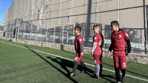 ثلاثة أطفال يقفون في ملعب كرة قدم ويرتدون قمصاناً حمراء، ويصطفون في انتظار تنفيذ ضربات الجزاء. - BBC News