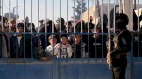 رجل يقف أمام البوابة وخلف قضبانها مجموعة من الأشخاص. - EPA