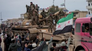 عناصر من الجيش السوري في دير حافر بعد انسحاب قوات سوريا الديمقراطية (قسد)، يقفون على ظهر دبابة ويحملون العلم السوري ذو النجوم الحمراء الثلاثة وحولهم حشد من الناس. - EPA