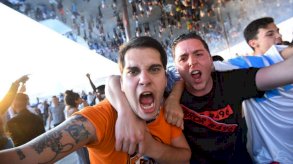 مشجعان يغمران بعضهما في مباراة لكرة القدم، ويصرخان، على اليمين شاب بقميص أسود وعلى اليسار شاب بقميص برتقالي مع وشم لفريق ماريسيليا الفرنسي على ذراعه - Getty Images