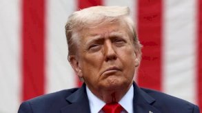 دونالد ترامب مرتديا بذلة وكرافت أحمر وخلفه علم الولايات المتحدة الأمريكية - Reuters