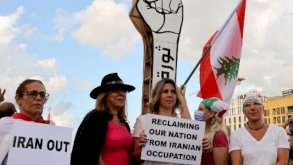 متظاهرون يتجمعون أمام رمز 'قبضة الثورة' لانتفاضة أكتوبر 2019، خلال تجمع في ساحة الشهداء بالعاصمة بيروت في 17 أكتوبر 2021، يحملون لافتات تطالب بإخراج نفوذ إيران من لبنان