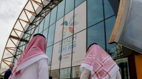 رجلان سعوديان أمام واجهة تحمل شعار إكسبو الرياض 2030