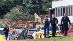 رجال شرطة ومسؤولون يسيرون في جبل مونغانوي بمدينة تاورانجا، حيث تسببت الأمطار في انهيار أرضي، بينما تواصل فرق الإنقاذ المحلية عمليات البحث عن المفقودين، في 22 يناير/كانون الثاني عام 2026 - 