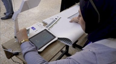 سيدة في لجنة الانتخابات في العراق تتحقق من هوية مقترع. - BBC