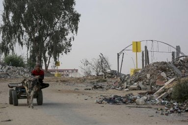 رجل فلسطيني يركب عربة يجرها حمار قرب حاجز خرساني (من الخلف) يُشير إلى